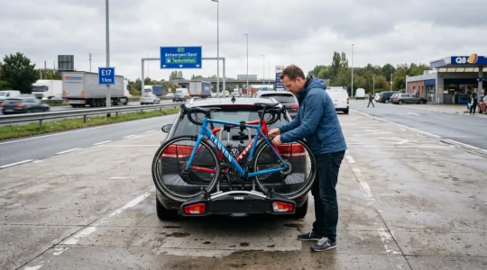Un automobiliste resserre les sangles d'un porte-vélos sur attelage chargé de deux vélos, sur une aire d'autoroute belge