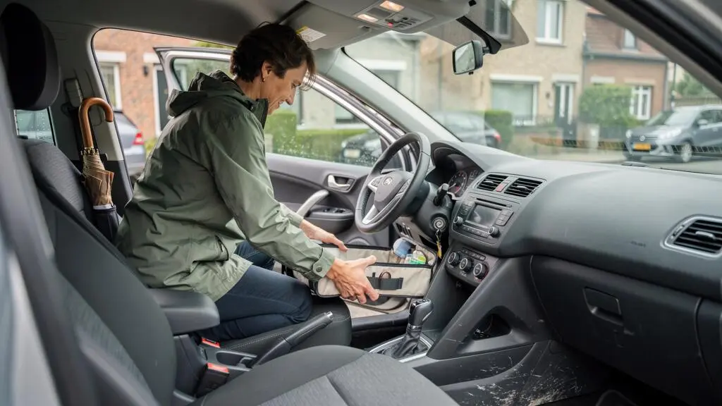 Une personne réorganise l'habitacle de sa voiture en plaçant un rangement souple dans le coffre, tableau de bord dégagé